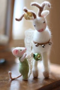 two small stuffed animals standing next to each other on a wooden table, one with a bell around it's neck