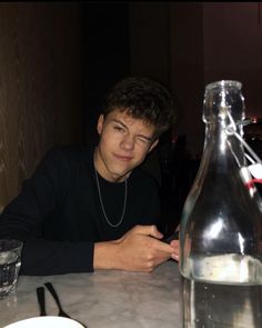 a young man sitting at a table next to a bottle