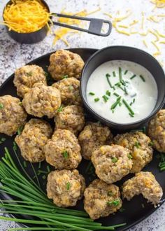 a black plate topped with meatballs next to a bowl of ranch dressing