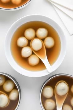 three bowls filled with soup and spoons on top of a white tablecloth next to two silver cups