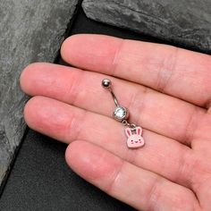 a person is holding a tiny pink bunny belly button navel bar in their left hand