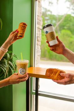 two people holding coffee cups and croissants in their hands while another person holds a piece of bread