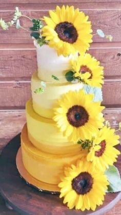 a three tiered cake with sunflowers on the top and bottom, sitting on a wooden table