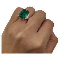 a person's hand holding an emerald and diamond ring