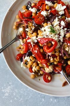 a white plate topped with vegetables and feta cheese next to a fork on a table