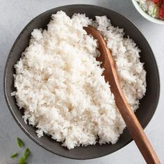 white rice in a bowl with a wooden spoon next to it on a counter top