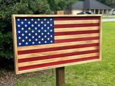 a wooden sign with an american flag painted on it in front of some grass and trees