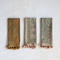 three pieces of cloth with tassels hanging from the side on a white wall