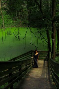 a woman standing on a wooden bridge over a swampy area with green algae growing in the water