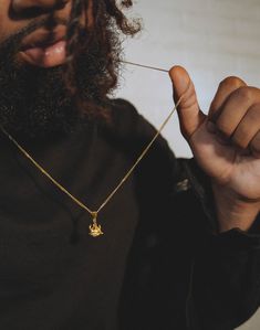 a man wearing a black shirt and holding a gold necklace with a small bird on it