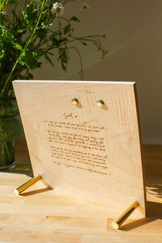 a wooden plaque with writing on it sitting next to a vase filled with white flowers