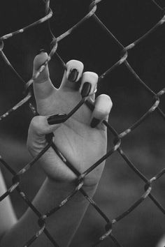 a person holding their hand up through a chain link fence with nails on the thumb