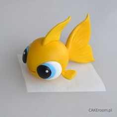 a yellow fish with big blue eyes sitting on top of a piece of white paper