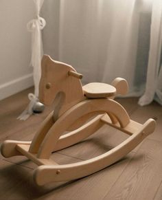 a wooden rocking horse toy sitting on the floor in front of a curtained window