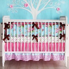 a baby crib with a tree painted on the wall and pink bedding set