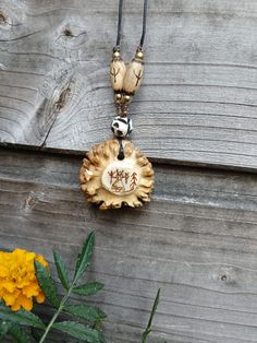 a wooden necklace with a bird on it hanging from a wood wall next to yellow flowers