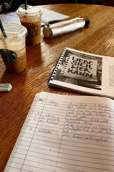 an open notebook sitting on top of a wooden table next to a cup of coffee