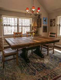 a dining room table with four chairs and a rug in front of the window that overlooks trees