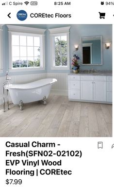 a white bath tub sitting next to a window in a blue and white bathroom with wood flooring