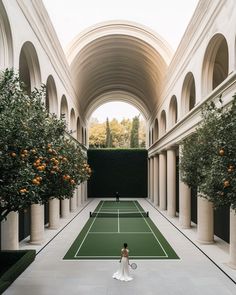 a woman standing on a tennis court holding a racquet in front of an orange tree