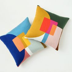 two colorful pillows sitting next to each other on top of a white surface and one has an abstract design