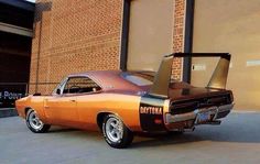 an orange muscle car parked in front of a brick building with its door open and the word daytona painted on it