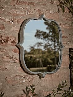 a mirror on the side of a brick wall with trees in the backround