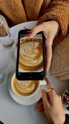 a woman is taking a photo with her cell phone while sitting in front of a cup of coffee