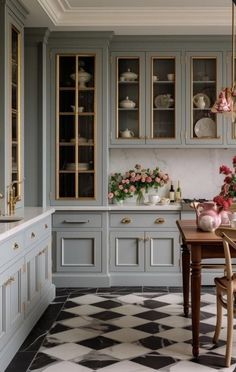 a kitchen with checkered flooring and cabinets in grey tones, pink flowers are on the table