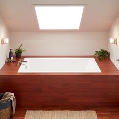 a bath tub sitting under a window next to a wooden counter top with potted plants on it