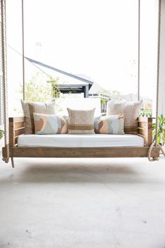 a wooden swing bed with pillows on it in the middle of a porch or patio