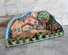 a ceramic sculpture with houses and trees on it's sides, in front of a stone wall