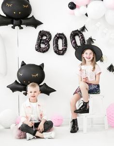 two children sitting in front of black and white balloons with the words boo on them