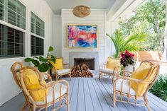 a porch with wicker chairs and yellow cushions on it, next to a fire place