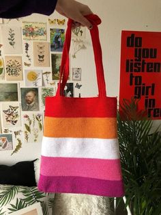 a person holding a red and white striped tote bag in front of a wall with pictures on it