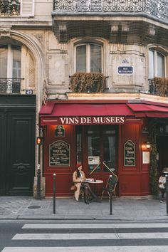 a woman sitting at a table in front of a red building on the side walk