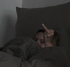 a woman laying in bed with her hand up to her face and pointing at something