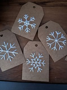 four tags with white snowflakes on them sitting on a wooden table next to a laptop