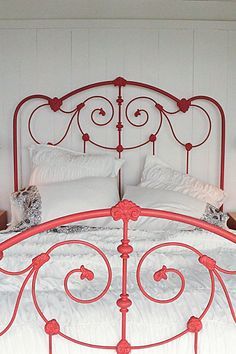 a white bed with red iron headboard and foot board in a room that has white walls