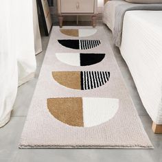 a white rug with black, brown and beige shapes on it next to a bed