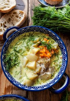 two bowls filled with soup on top of a wooden table next to bread and vegetables