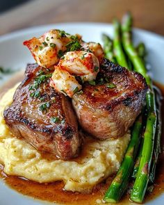 some meat and mashed potatoes on a plate with asparagus in the foreground