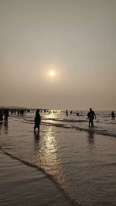 many people are walking on the beach at sunset or sunrise, and one person is standing in the water