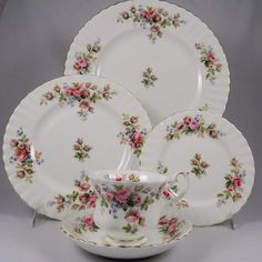 a set of four china plates with pink flowers and leaves on the rim, each plate has a matching saucer