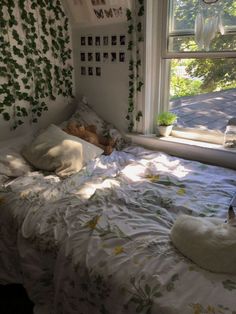 an unmade bed in front of a window with ivy growing on the wall behind it