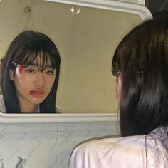 a woman looking at herself in the mirror with blood on her face and cheek,