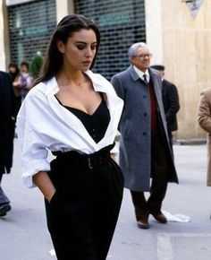 a woman in black pants and white shirt walking down the street with other people behind her