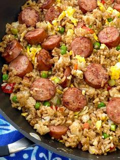 a skillet filled with rice and sausages on top of a blue table cloth