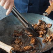 a person cooking food on top of a grill with tongs in their hand and another person holding a spatula