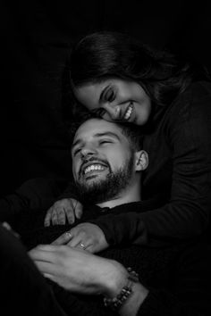 a man and woman cuddle together in the dark, smiling at each other's eyes